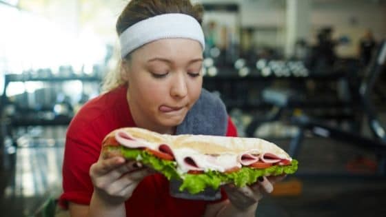 Woman eating a huge sandwich while exercising at the gym